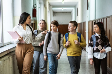 The teacher walks through the school lobby while speaking with her students as class is about to begin. The moment feels relaxed and friendly, with everyone easing into the school day.