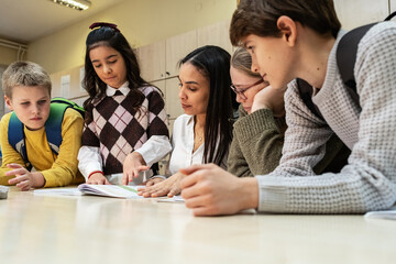 A small group of students is in their elementary classroom while a mixed-race teacher guides them through a math and geometry lesson. She is asking questions and helping them stay focused as they work