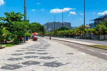 Sidewalk with mosaic of Beach in Barra da Tijuca, Rio de Janeiro, Brazil. Sunny cityscape of Rio de Janeiro.