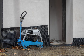 A small plate compactor with a handle near a new building.
