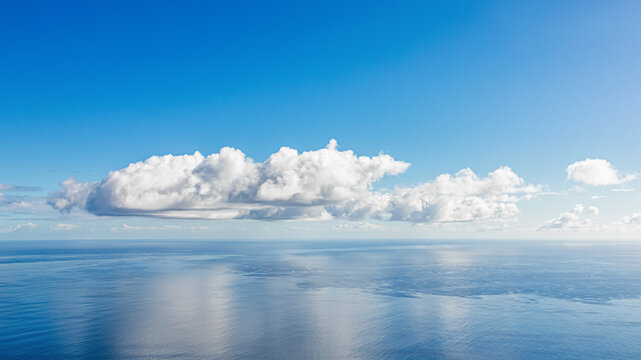 Cloudy seascape. Beautiful abstract nature background in blue tones showing large white clouds over blue ocean water, with a clear blue sky in the background