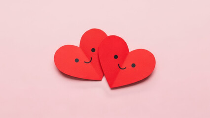 Two red paper hearts with smiling faces on a pink background.