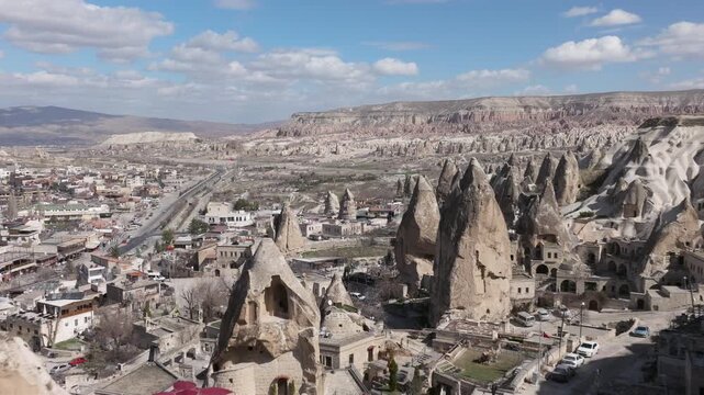 Aerial drone footage of G&ouml;reme town in Cappadocia, Turkey, surrounded by fairy chimneys and volcanic rock formations. The shot reveals traditional stone houses, cave dwellings carved into soft tuff ro