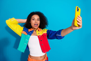 Colorful jacket selfie by a young woman smiling while taking a photo against a blue background