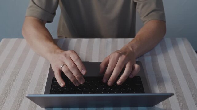 Close up top view of male hands typing on a laptop keyboard. Natural hand placement, smooth finger motion and calm everyday computer activity at home. High quality 4k footage