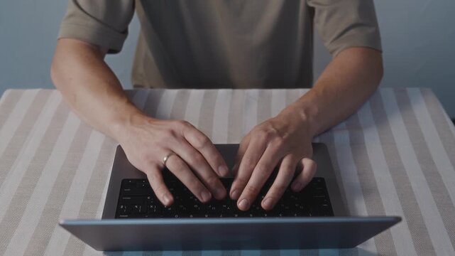 Centered top angle close up of male hands typing on a laptop keyboard. Symmetrical composition, relaxed posture and focused digital work in a quiet indoor space. High quality 4k footage