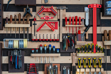 Various old work tools hang on the wooden wall in a home carpentry workshop, close up. Wall French cleat system to hang work tools