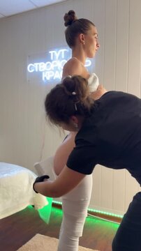Professional cosmetologist applies compression body wrap to hips and buttocks of young woman in modern spa salon during body shaping and anti cellulite wellness procedure