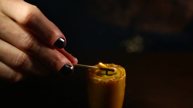 Woman hand lights a match the bees wax candle for mood, relaxation, meditation dark black background. Person lighting the decoration handmade single candle flame. Closeup