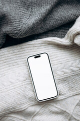 Smartphone mockup on folded gray and white sweaters, flat lay.