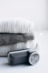 Gray and white sweaters with fabric shaver on festive background.