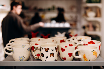 Colorful printed cups on handmade tableware store shelf with space for text.
