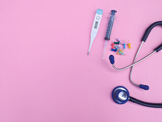 medical tools on pink background with stethoscope, syringe, thermometer, and colorful push pins for healthcare concept