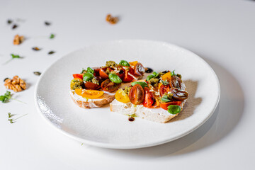 Minimal food styling of bruschetta with cream cheese, cherry tomatoes, basil and pesto on white...