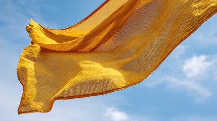 Yellow fabric flowing in wind against blue sky