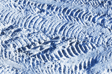 Tire tracks in fresh snow. Winter road surface closeup. Repeating pattern of car tread marks. Cold weather texture background. Frozen ground detail. Driving in winter conditions.