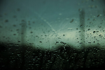 Obraz premium Macro view of raindrops on a car windshield with blurred trees behind. Captures the texture of water droplets during a rainy day in natural light.