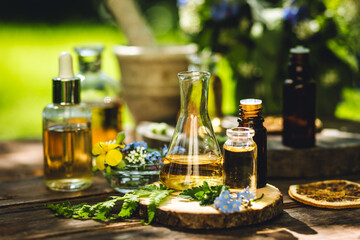 Mix of holistic flowers and herbs, salt, massage herb-infused essential oil in glass bottles. Aromatherapy, fragrance production. Herbal pure natural cosmetic ingredients on wooden background