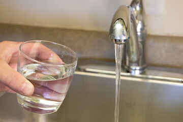 Drinking Water From Kitchen Faucet.Close up of hand holding glass under kitchen faucet with running...