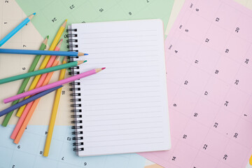 Open notebook with colored pencils on calendar background. Creative planning and time management.