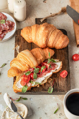 Croissant sandwich with salami, sausage, cherry tomatoes, soft cheese and chard micro greens on wooden board kitchen table background for savory healthy breakfast