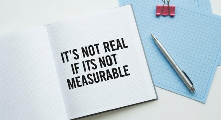 Open notebook with a bold quote about measurability sits on a desk next to a pen and clips
