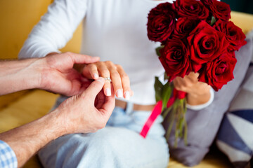 Romantic indoor moment as couple exchanges a ring while a bouquet of red roses is held nearby, capturing love, commitment, and celebration