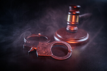 Gavel and handcuffs on a dark surface surrounded by smoke, symbolizing justice and law enforcement, creating a dramatic and intense atmosphere for legal themes