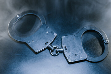 Black handcuffs lying on a dark surface with a smoky background, symbolizing law enforcement, justice, and restraint in a dramatic and intense atmosphere