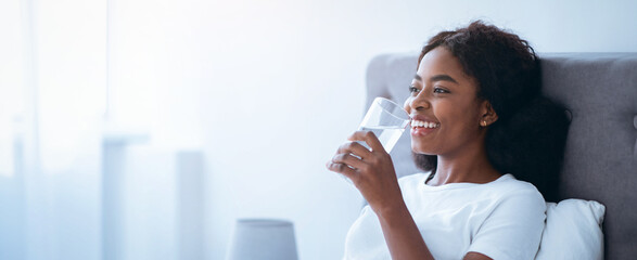 A person sits comfortably in a soft chair, smiling while holding a glass of water. Natural light...