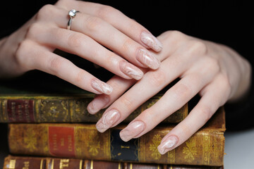 Two hands with long, decorated nails are placed on top of stacked, old books. 