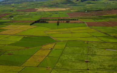 Panoramic view of the colorful agricultural fields from Serra do Cume lookout on Terceira Island, Azores, Portugal. Lush green, yellow, and brown farmlands form a scenic patchwork landscape 