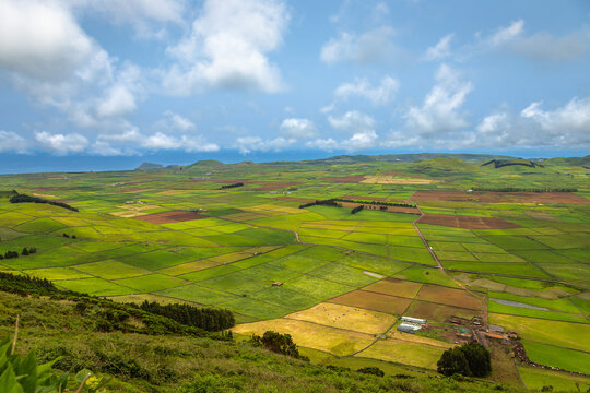 Panoramic view of the colorful agricultural fields from Serra do Cume lookout on Terceira Island, Azores, Portugal. Lush green, yellow, and brown farmlands form a scenic patchwork landscape 