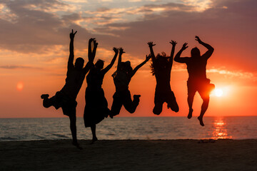 Silhouette of five people jumping with joy on the seashore during a warm and colorful summer sunset at the beach