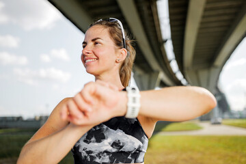 Running woman checks her watch under a bridge
