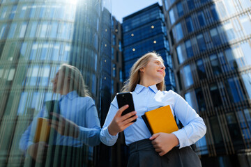 Person holds a phone and a notebook outside a building