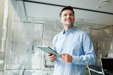 Young man smiles while holding a tablet in an office space