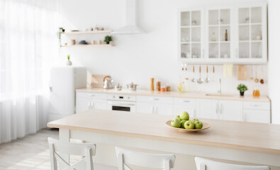 Scandinavian interior of kitchen with wooden island and white chairs nearby, various utensils and dishes on light kitchen furniture, shelves with spices. Blurred background