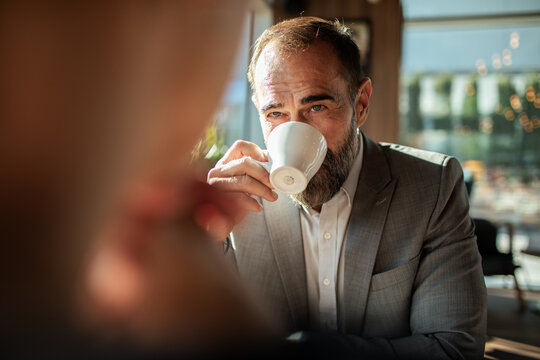 Mature man in suit sipping coffee at cafe, pensive