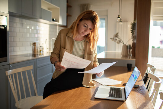 Adult woman reviewing bills with concerned look in home kitchen
