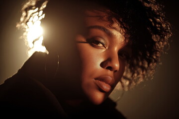 Woman with curly hair in low light setting near bright background during an indoor session