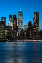 A dramatic view of the downtown Manhattan skyline at night, featuring the brightly illuminated skyscrapers.
