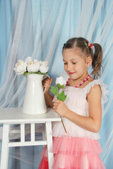 Little girl with a bouquet of white roses on a white table near a blue curtain