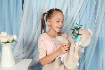 Cute Caucasian girl smiling while holding a plush rabbit in her arms on blue background