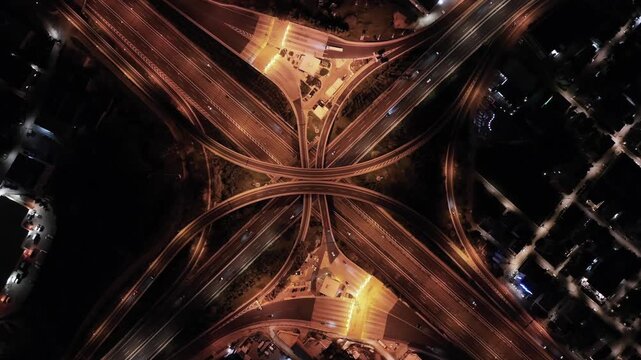 Aerial drone top down hyper lapse loop night video of illuminated urban elevated road junction and interchange overpass in city with light traffic