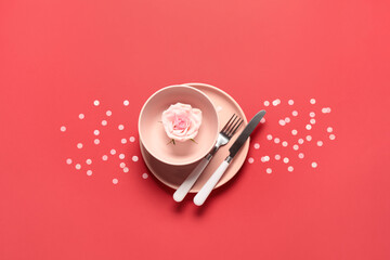 Beautiful table setting for Valentine's Day with rose flower and confetti on red background