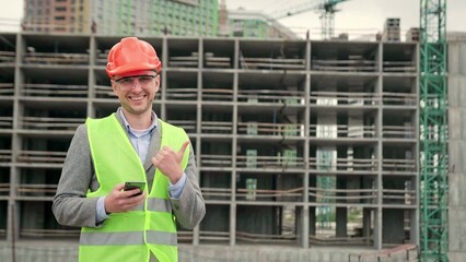 Cheerful construction supervisor posing for camera against new building
