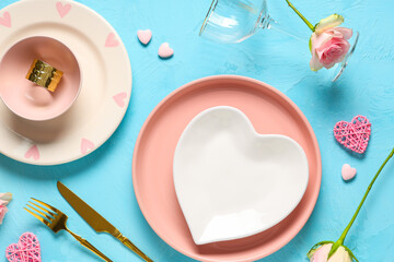 Table setting for Valentine's Day with rose flowers and decorative hearts on blue background