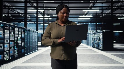 Supervisor in data center using laptop to coordinate deployment of new server architecture. Server farm IT specialist using notebook to do rollout of cybersecurity framework, protecting data, camera A