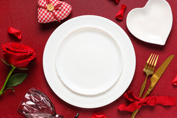 Table setting for Valentine's Day with rose flower, decorative heart and petals on red background